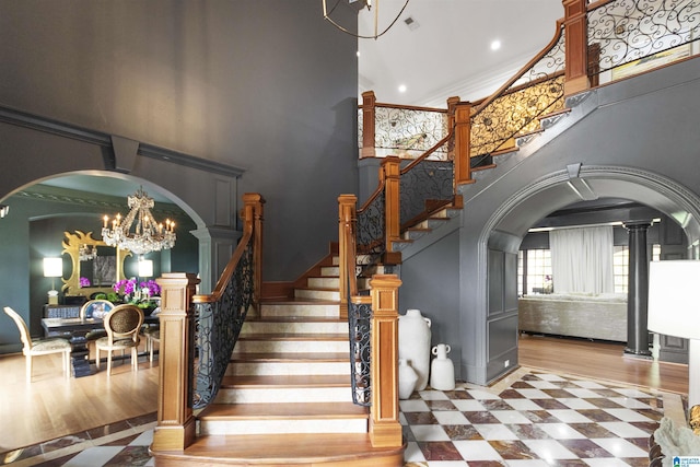 stairway with recessed lighting, a towering ceiling, wood finished floors, arched walkways, and a notable chandelier