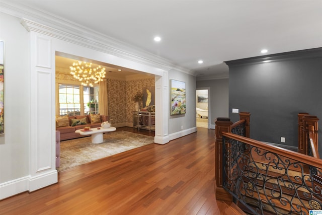 hall with recessed lighting, an inviting chandelier, wood finished floors, ornamental molding, and an upstairs landing