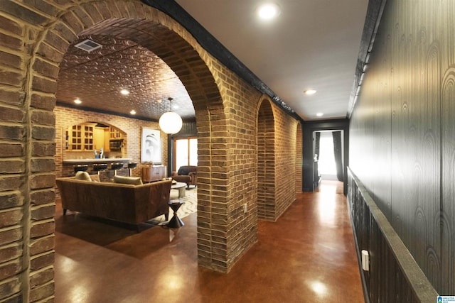hallway featuring arched walkways, plenty of natural light, visible vents, brick wall, and concrete floors