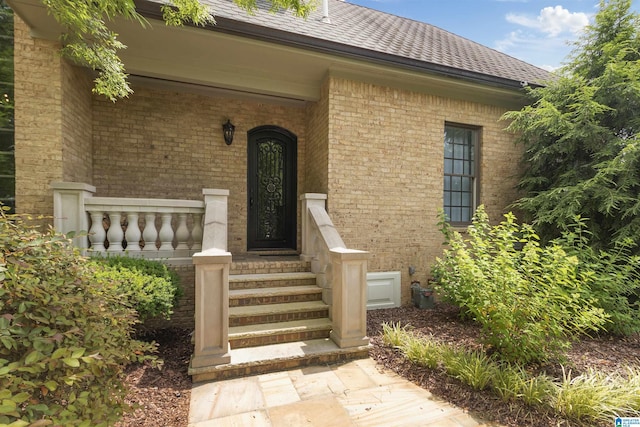 doorway to property with brick siding and a shingled roof