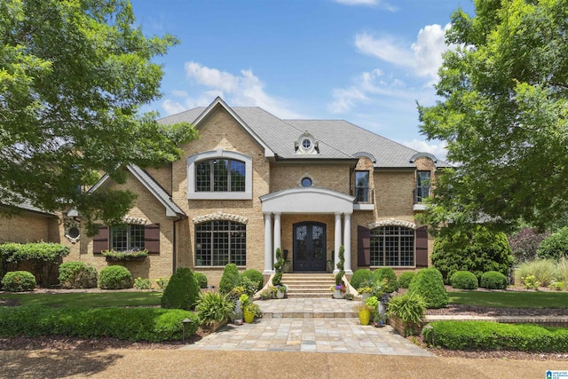 french country inspired facade with a front lawn, french doors, and brick siding