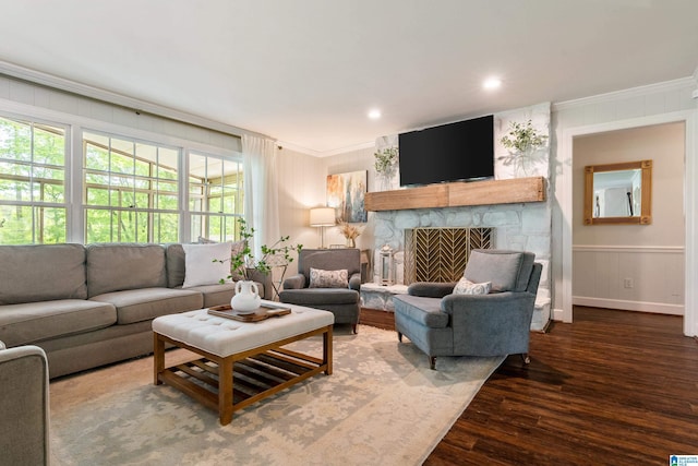 living area featuring wood finished floors, a decorative wall, a stone fireplace, baseboards, and crown molding