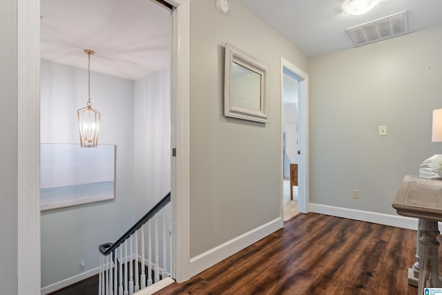 hall featuring dark wood-style floors, visible vents, an inviting chandelier, and baseboards