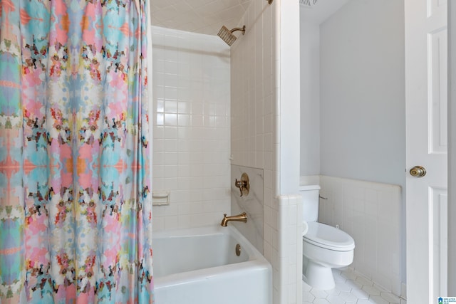 bathroom featuring tile patterned floors, wainscoting, shower / tub combo, and toilet