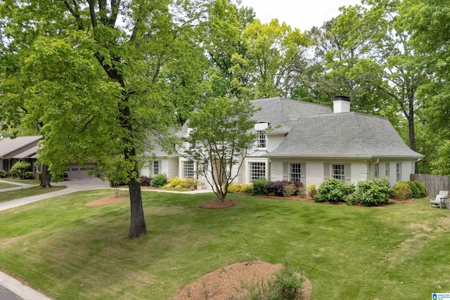 view of front of home with fence, a chimney, a front yard, and a shingled roof