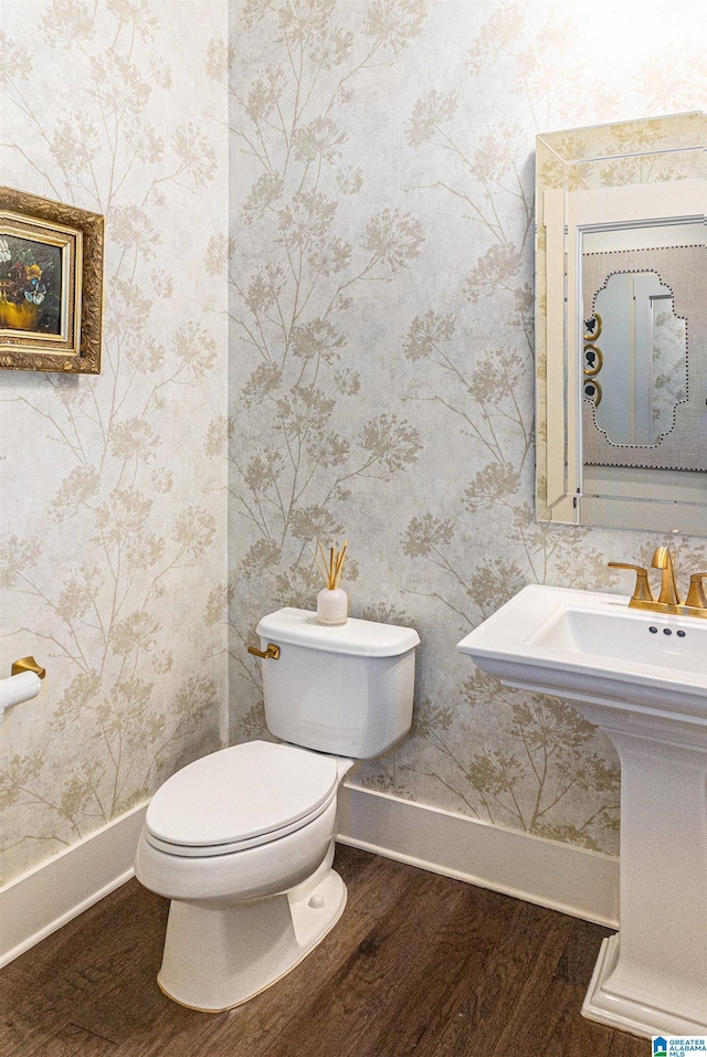 bathroom featuring baseboards, wallpapered walls, wood finished floors, and toilet