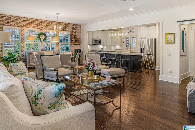 living area featuring dark wood-style flooring, brick wall, a notable chandelier, crown molding, and baseboards