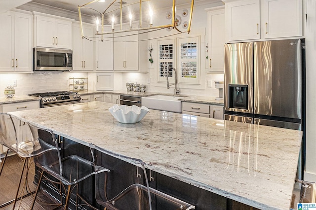 kitchen featuring appliances with stainless steel finishes, backsplash, a sink, white cabinetry, and a kitchen breakfast bar