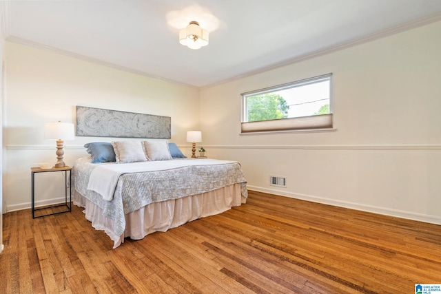bedroom featuring baseboards, ornamental molding, wood finished floors, and visible vents