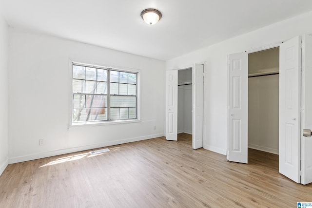 unfurnished bedroom with two closets, baseboards, visible vents, and light wood finished floors