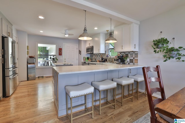 kitchen featuring a peninsula, light wood-style floors, a healthy amount of sunlight, and appliances with stainless steel finishes