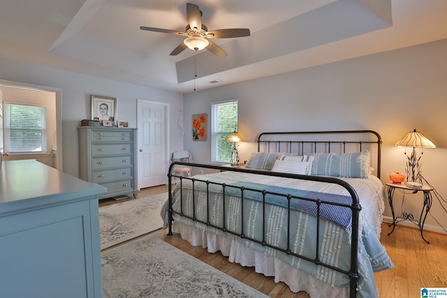 bedroom featuring a raised ceiling, light wood-type flooring, visible vents, and ceiling fan