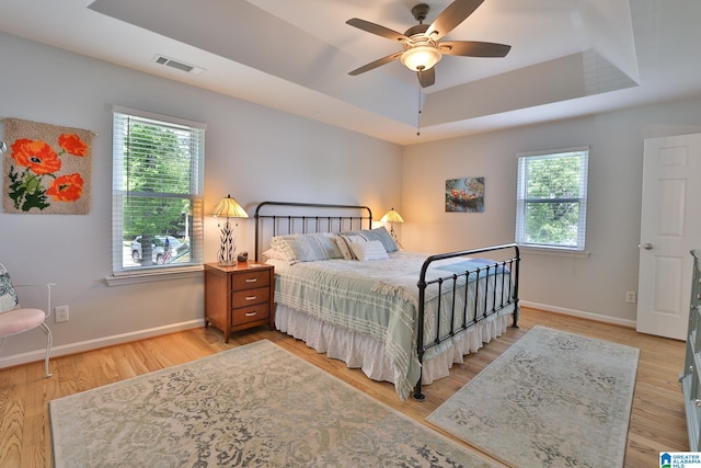 bedroom with baseboards, multiple windows, a tray ceiling, and visible vents