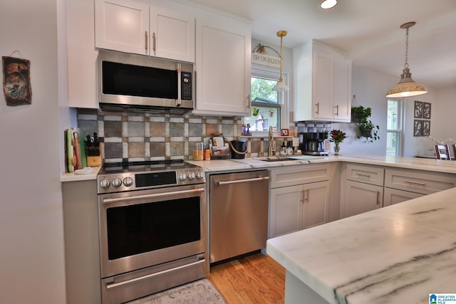 kitchen with white cabinets, light wood-style floors, decorative backsplash, decorative light fixtures, and appliances with stainless steel finishes