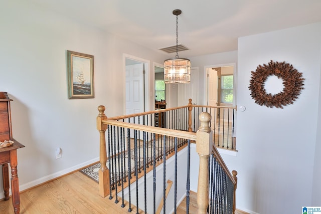 staircase with baseboards, wood finished floors, visible vents, and an inviting chandelier