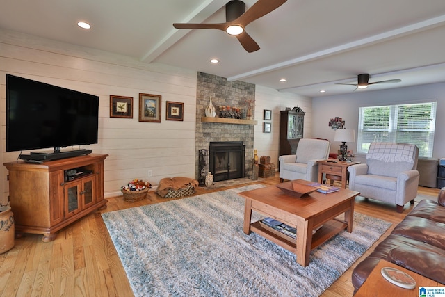 living area with a stone fireplace, a ceiling fan, beam ceiling, and light wood-style floors