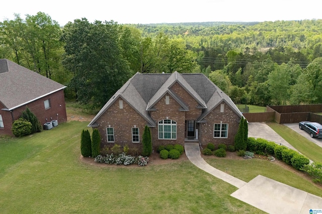 view of front of home with brick siding, a front yard, and a wooded view