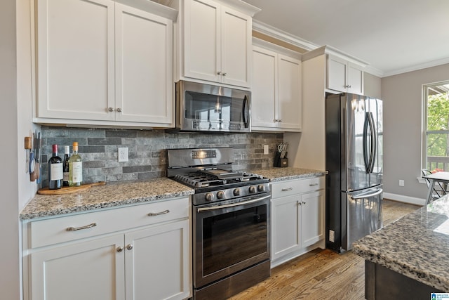 kitchen with light stone counters, light wood-style floors, crown molding, decorative backsplash, and appliances with stainless steel finishes