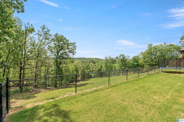 view of yard with a forest view, a trampoline, and fence private yard