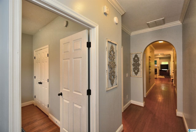 hallway featuring visible vents, ornamental molding, baseboards, dark wood-type flooring, and arched walkways