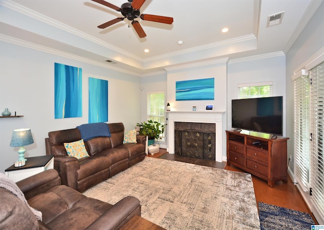 living area featuring ceiling fan, dark wood-style flooring, visible vents, a fireplace, and a raised ceiling