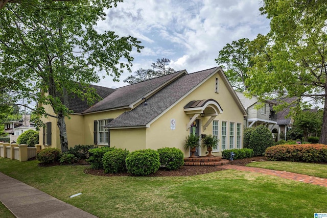 view of front facade with a shingled roof, a front lawn, and stucco siding