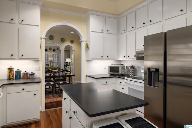 kitchen featuring dark wood finished floors, stainless steel appliances, under cabinet range hood, ornamental molding, and dark countertops