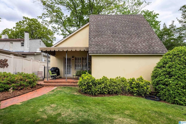 view of front of house featuring a shingled roof, fence, a front lawn, and stucco siding