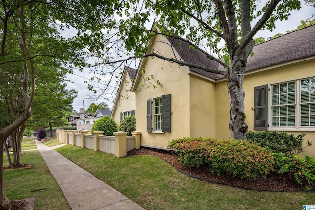 view of side of home with fence, stucco siding, and a lawn