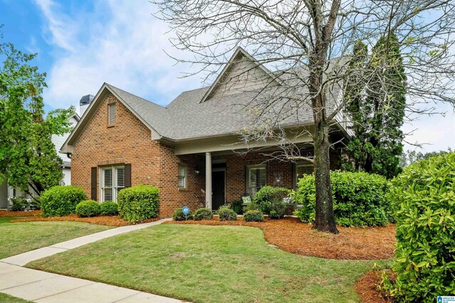 view of front facade with a front yard, a shingled roof, and brick siding