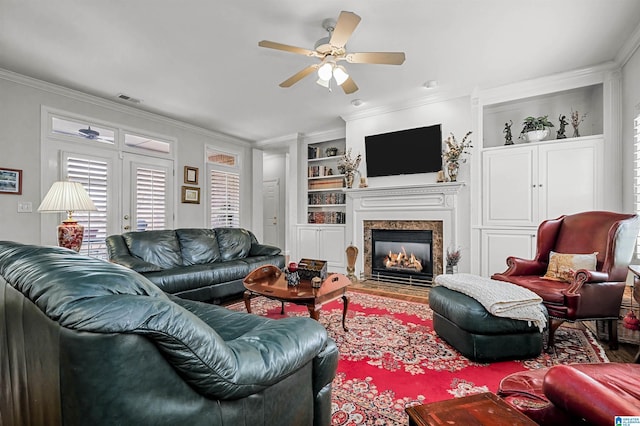 living area featuring ceiling fan, ornamental molding, built in features, visible vents, and a high end fireplace