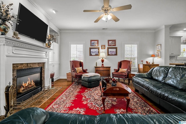 living area featuring wood finished floors, ceiling fan, a fireplace, visible vents, and crown molding