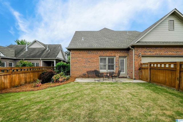 rear view of house featuring a shingled roof, a patio area, a yard, a fenced backyard, and brick siding