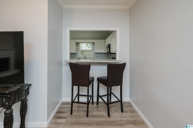 kitchen featuring crown molding, black microwave, light countertops, a kitchen breakfast bar, and light wood-style flooring