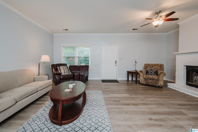 living room with crown molding, a ceiling fan, light wood-type flooring, and a brick fireplace