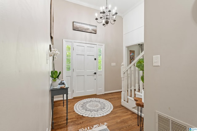 foyer featuring a notable chandelier, crown molding, visible vents, a towering ceiling, and wood finished floors