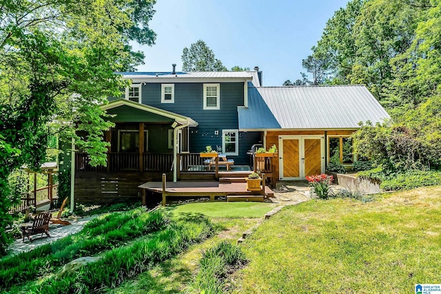 back of property with a chimney, a deck, metal roof, and a lawn