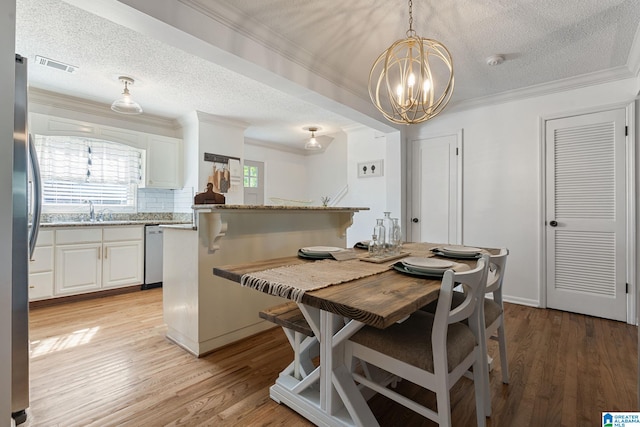 dining room featuring a chandelier, visible vents, light wood-style floors, and a textured ceiling
