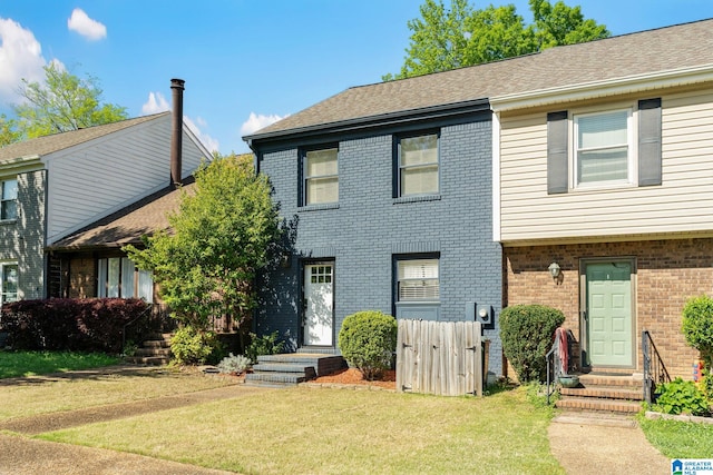 townhome / multi-family property featuring brick siding, fence, entry steps, and a front lawn