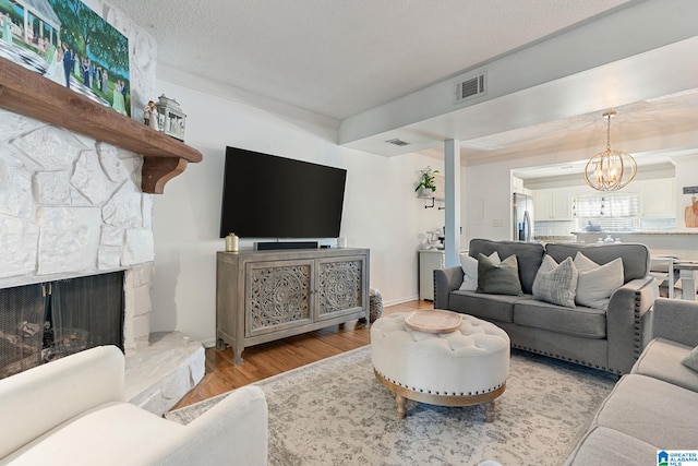 living room with a stone fireplace, visible vents, a chandelier, and wood finished floors
