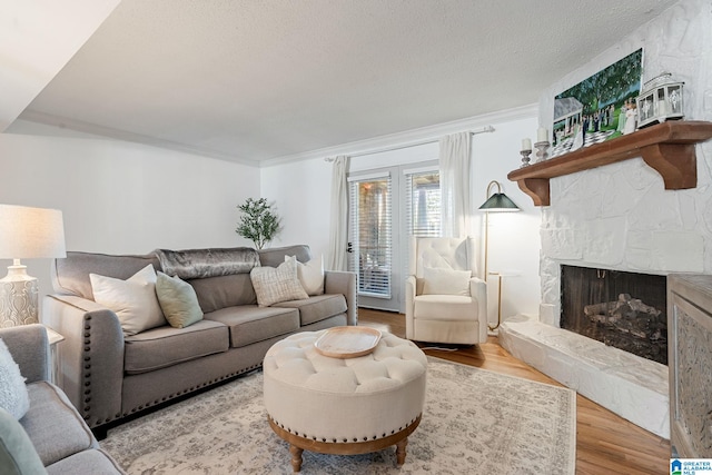 living area featuring a textured ceiling, wood finished floors, ornamental molding, and a stone fireplace