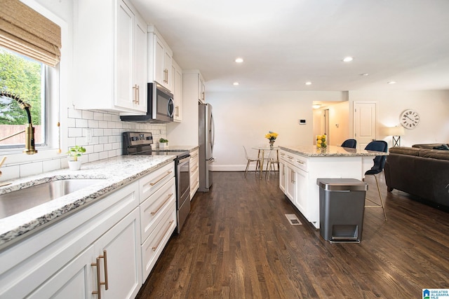 kitchen with dark wood-style floors, a sink, a breakfast bar area, white cabinetry, and appliances with stainless steel finishes