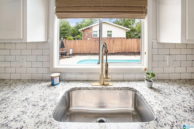 room details featuring light stone countertops, a sink, white cabinets, and backsplash