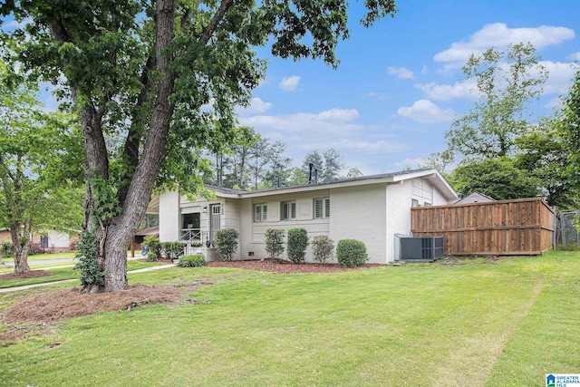 view of front of house with central AC, brick siding, fence, and a front yard