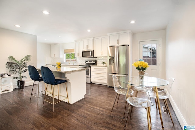 kitchen featuring decorative backsplash, a breakfast bar, stainless steel appliances, baseboards, and dark wood-type flooring