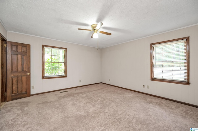 carpeted empty room featuring a ceiling fan, a healthy amount of sunlight, crown molding, and visible vents