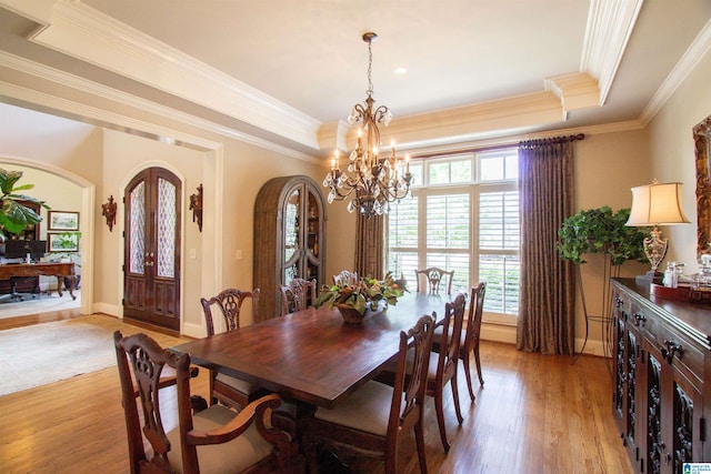 dining space with arched walkways, a tray ceiling, light wood-style flooring, ornamental molding, and a chandelier