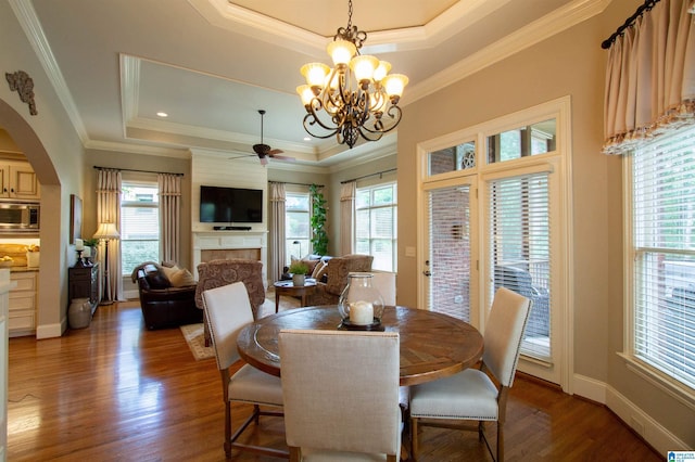 dining area with a raised ceiling, a fireplace, wood finished floors, arched walkways, and crown molding