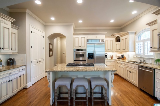 kitchen featuring stainless steel appliances, a sink, tasteful backsplash, light wood-style floors, and a center island