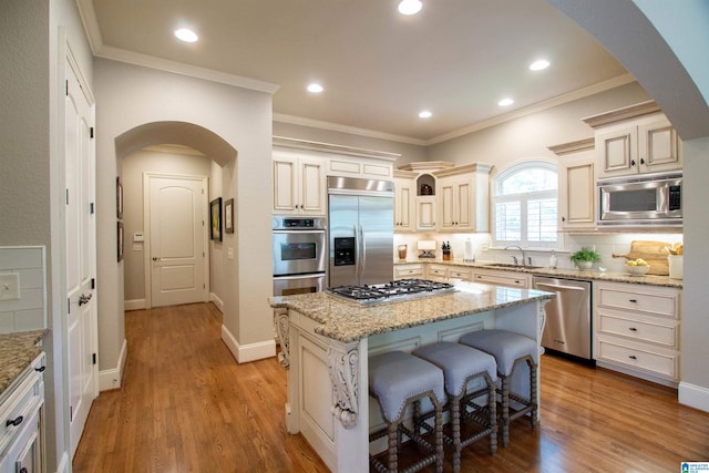 kitchen with built in appliances, arched walkways, a sink, a kitchen island, and crown molding